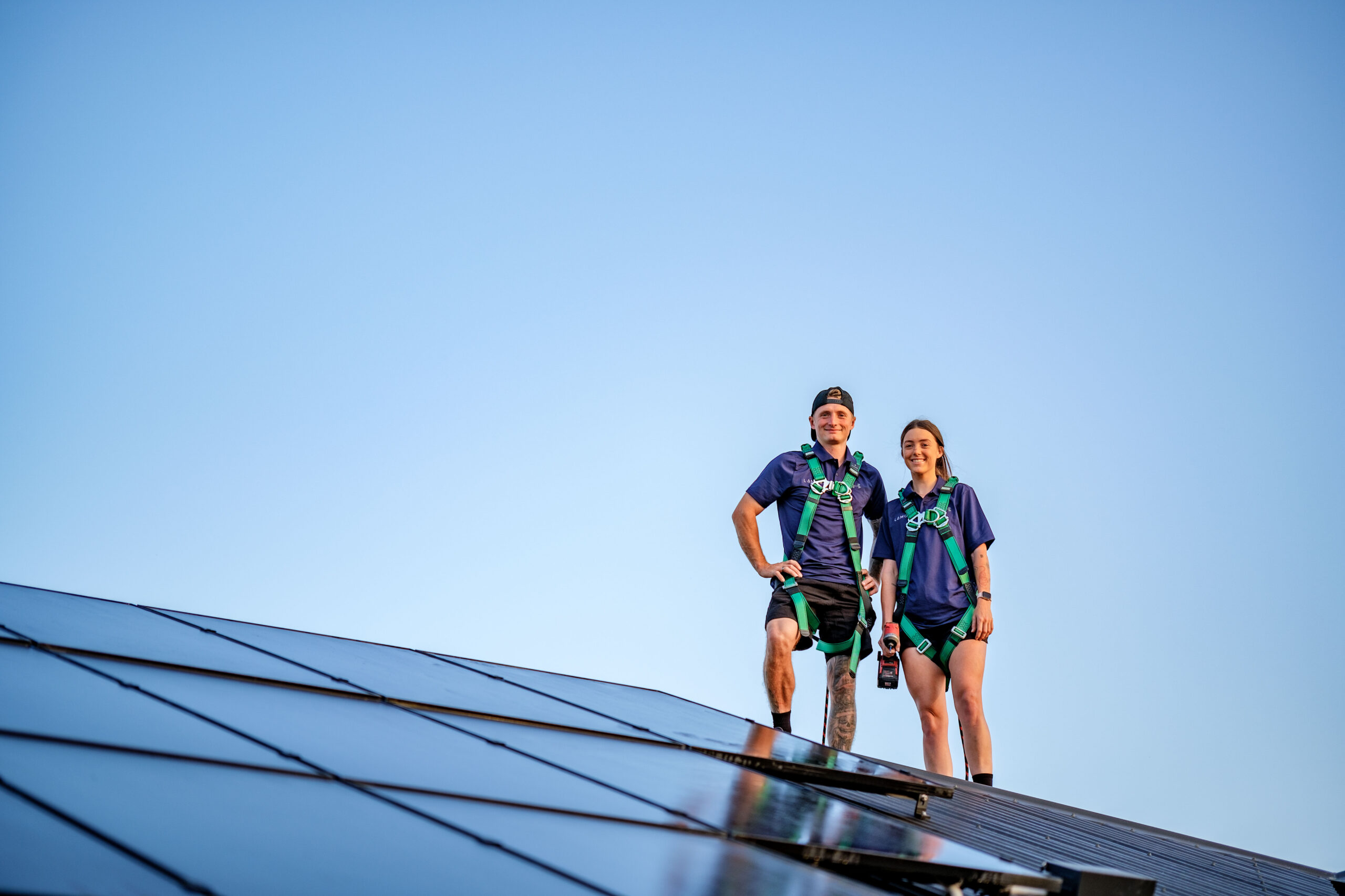 A duo of solar installers standing on a roof that has solar panels